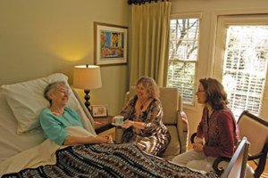 two women surrounding elder women in bed